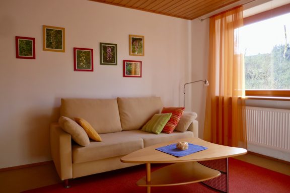 Wohnzimmer Gemütliches Wohnzimmer mit beigem Sofa, bunten Kissen und einer Fensterfront.