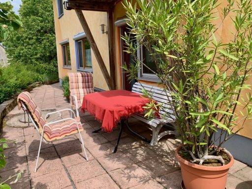 Terrasse Gemütliche Terrasse mit rotem Tisch, Bank und Pflanzen im Hinterhof.