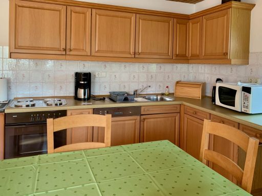 Wohnküche Holzfarbene Küche mit Gasherd, Mikrowelle und Tisch mit grünem Tischdecke.