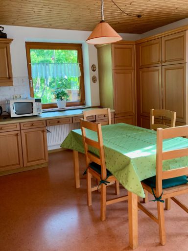 Wohnküche Helle Küche mit Holzschränken, einem Tisch mit grünem Tischtuch und Fenstersicht ins Freie.