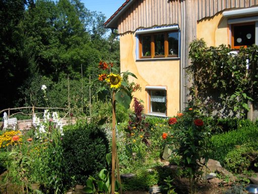 Ferienwohnung Blühender Garten mit Sonnenblumen und bunten Blumen vor einem gelben Haus.